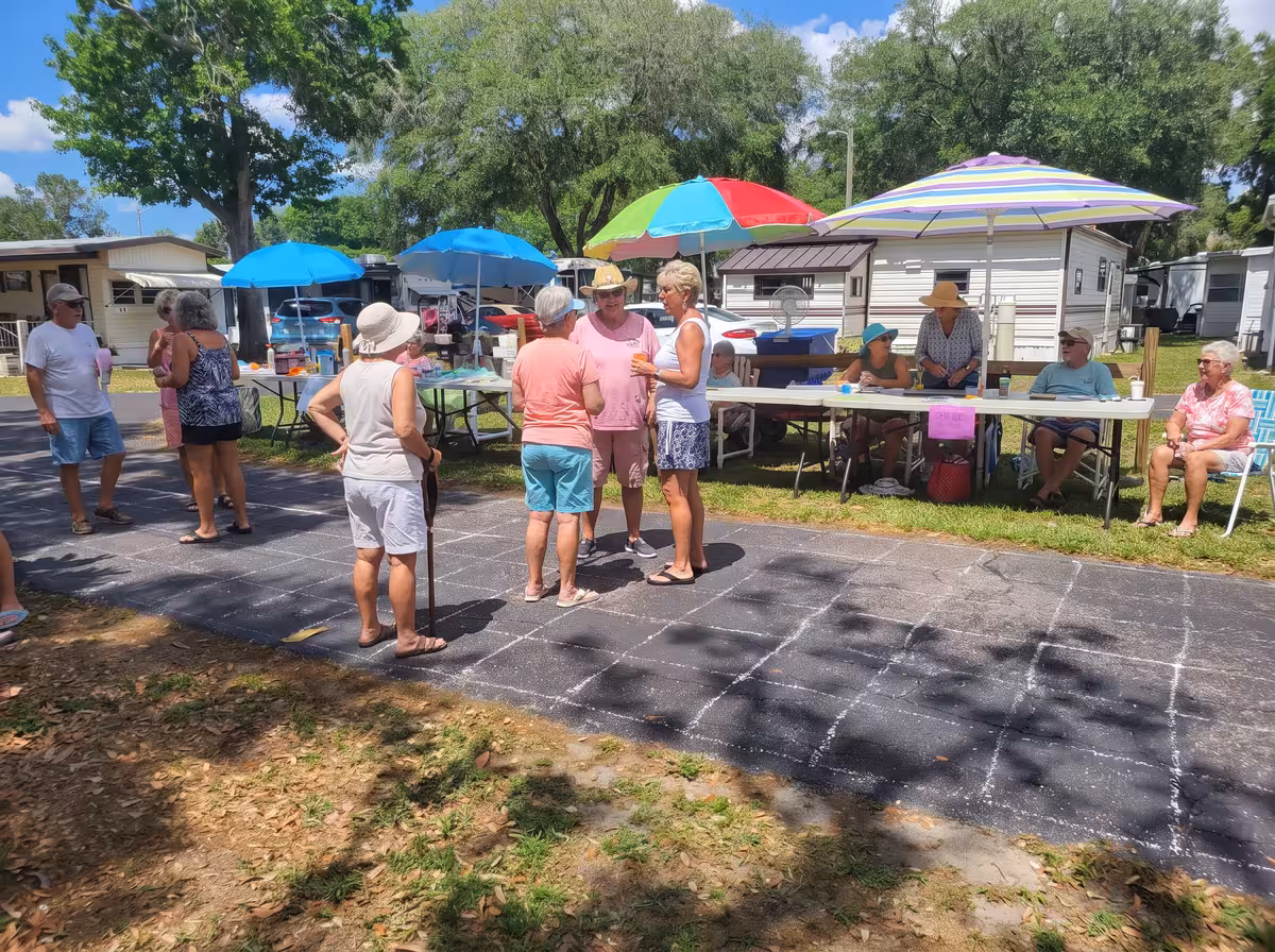 Residents socializing under colorful umbrellas beside a chalk shuffleboard court at an RV park