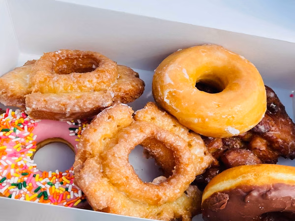 Box of assorted donuts including glazed, sprinkled, frosted, fritter, and chocolate varieties.