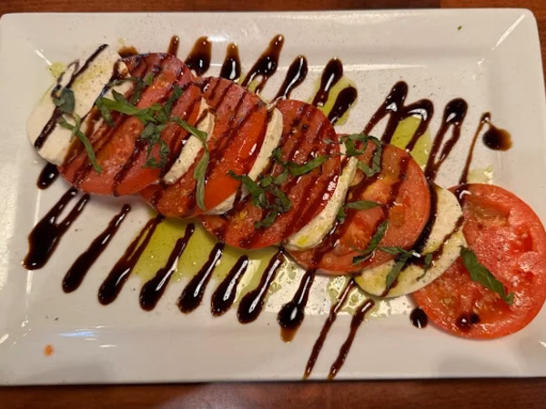 Caprese salad with tomato and mozzarella slices, basil, and balsamic drizzle on a white plate