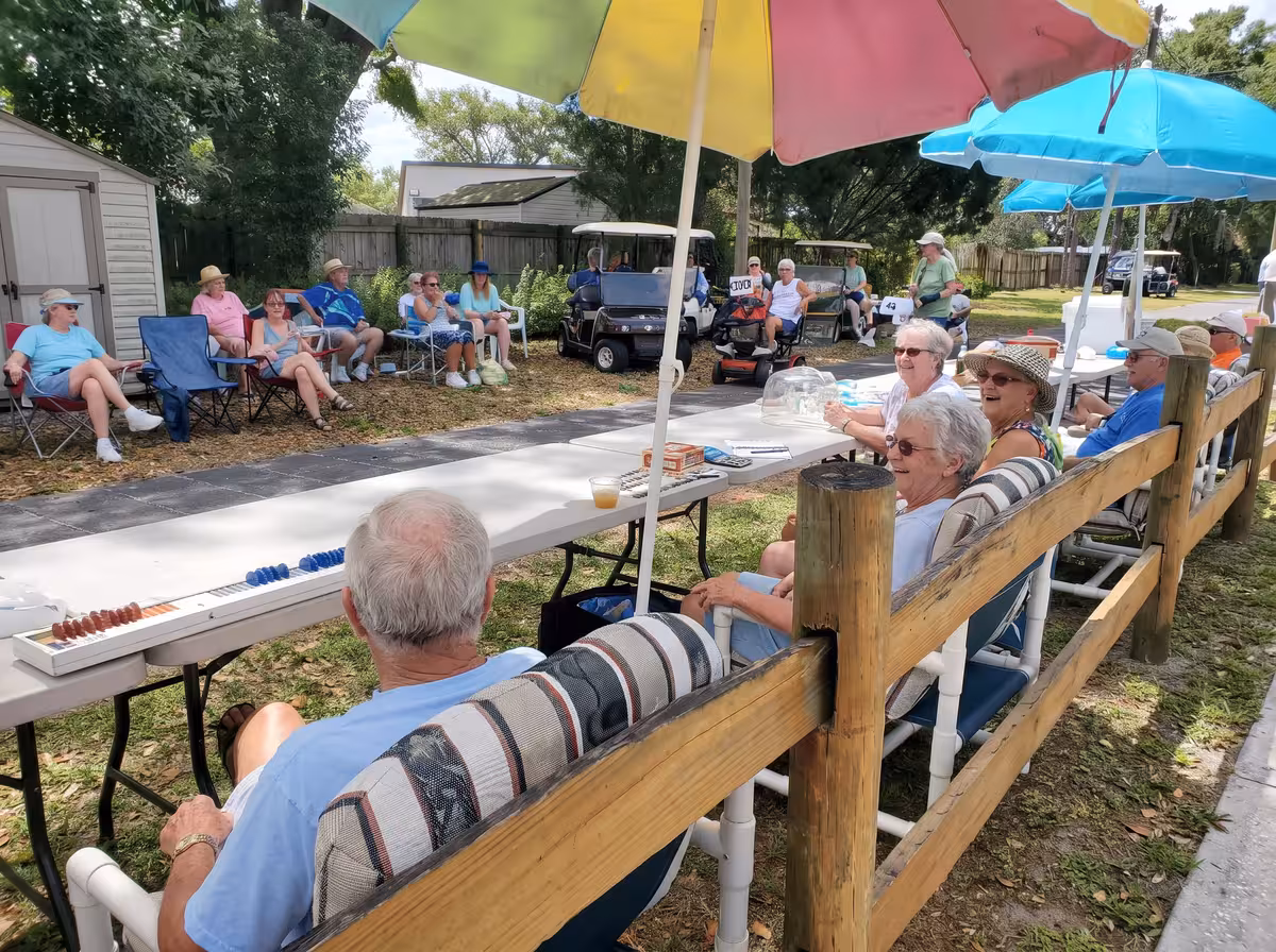 Seniors gathered under colorful umbrellas watching a shuffleboard game at an RV park