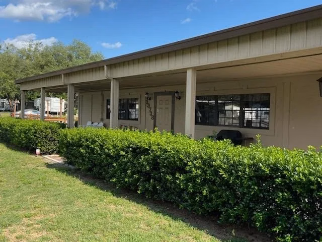 Covered clubhouse porch with grill and hedges at an RV park, with RVs parked in the background.