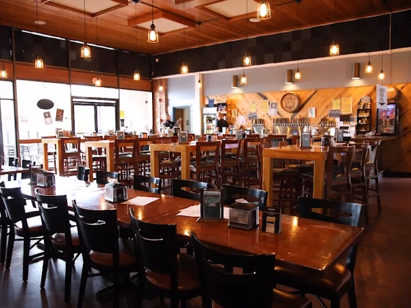 Restaurant interior with wooden tables, black chairs, pendant lights, and bar with beer taps