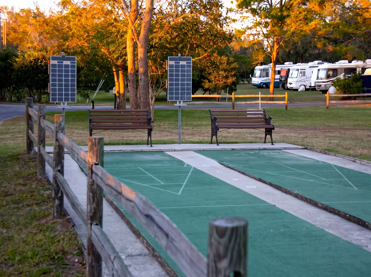 Shuffleboard courts with benches and parked RVs in the background at sunset
